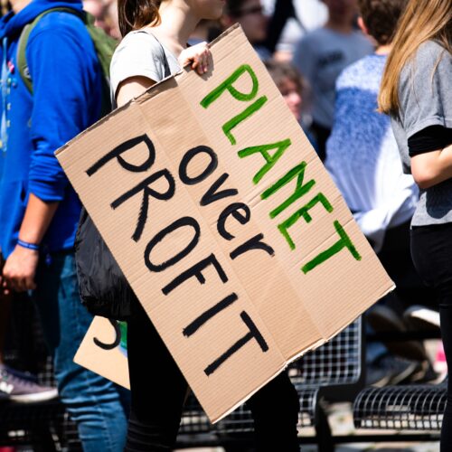 Idividual holding a 'Planet over Profit' placard in a city setting, symbolising environmental activism for green public relations